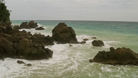 Aerial-drone-shot-over-waves-crashing-into-the-rocky-coastline-of-Banbanon-Beach,-Surigao-Del-Norte,-Philippines-on-a-cloudy-day