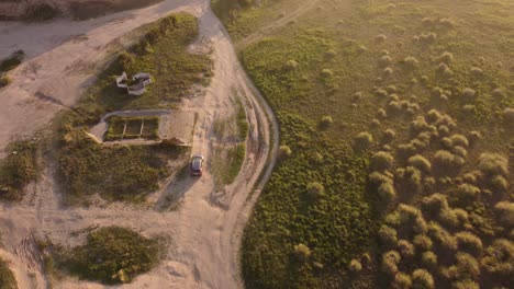 Aerial-tracking-shot-of-car-driving-on-rural-off-road-during-sunset-beside-green-landscape-in-Mar-del-Plata,Argentina