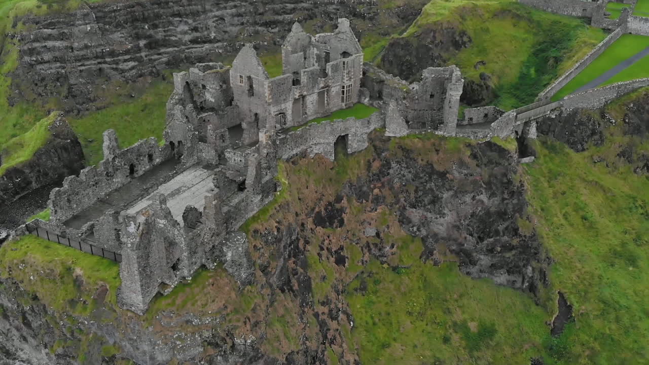 대서양 근처의 현무암 노두 가장자리에 있는 중세 성 유적 위로 날아가는 기울어진 하향식 드론 보기