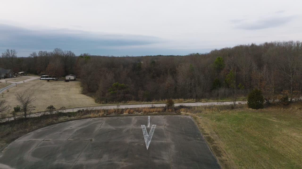 Flyover above small decommissioned airport runway in rural Arkansas, past end, over bare trees, towards small pond.