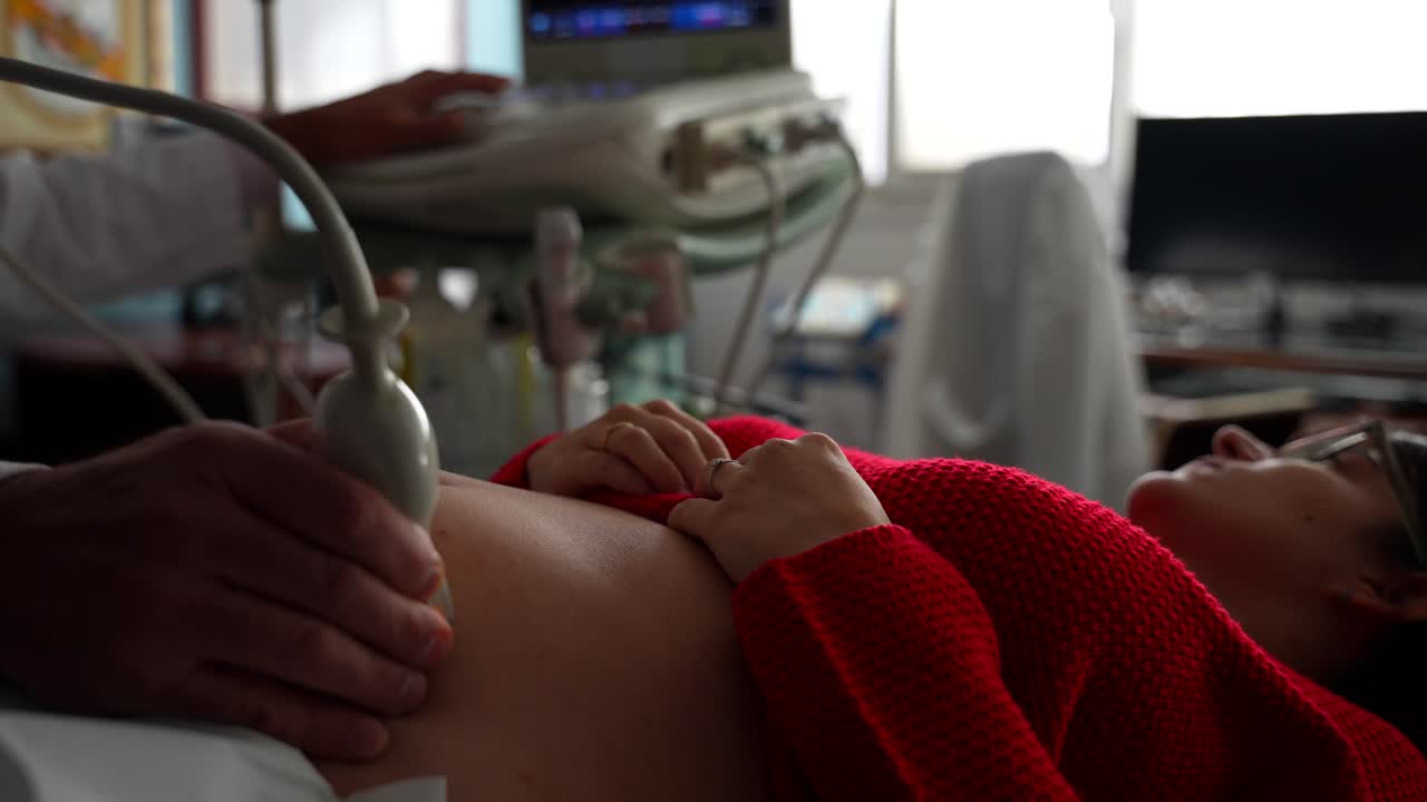 mujer embarazada acostada en una camilla mirando la pantalla de ultrasonido mientras el ginecólogo escanea su vientre