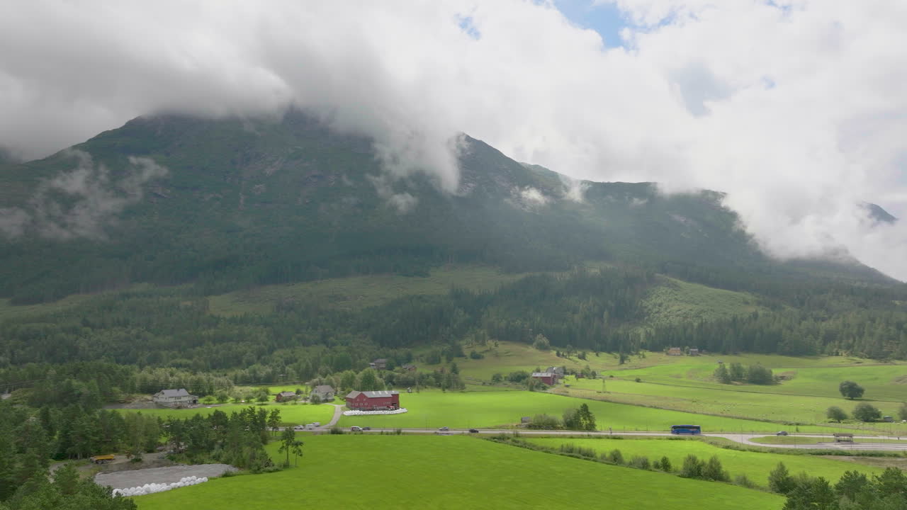 vista aérea de la carretera rural que cruza los verdes campos agrícolas que revelan el fondo del paisaje del fiordo, noruega