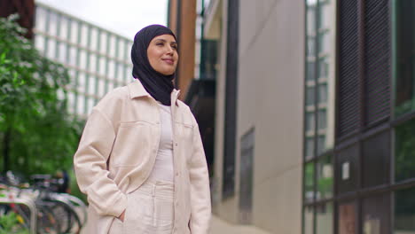 porträt einer modernen muslimischen geschäftsfrau mit hijab und geschäftsanzug, die vor einem bürogebäude mit der hand in der tasche steht und zur arbeit geht