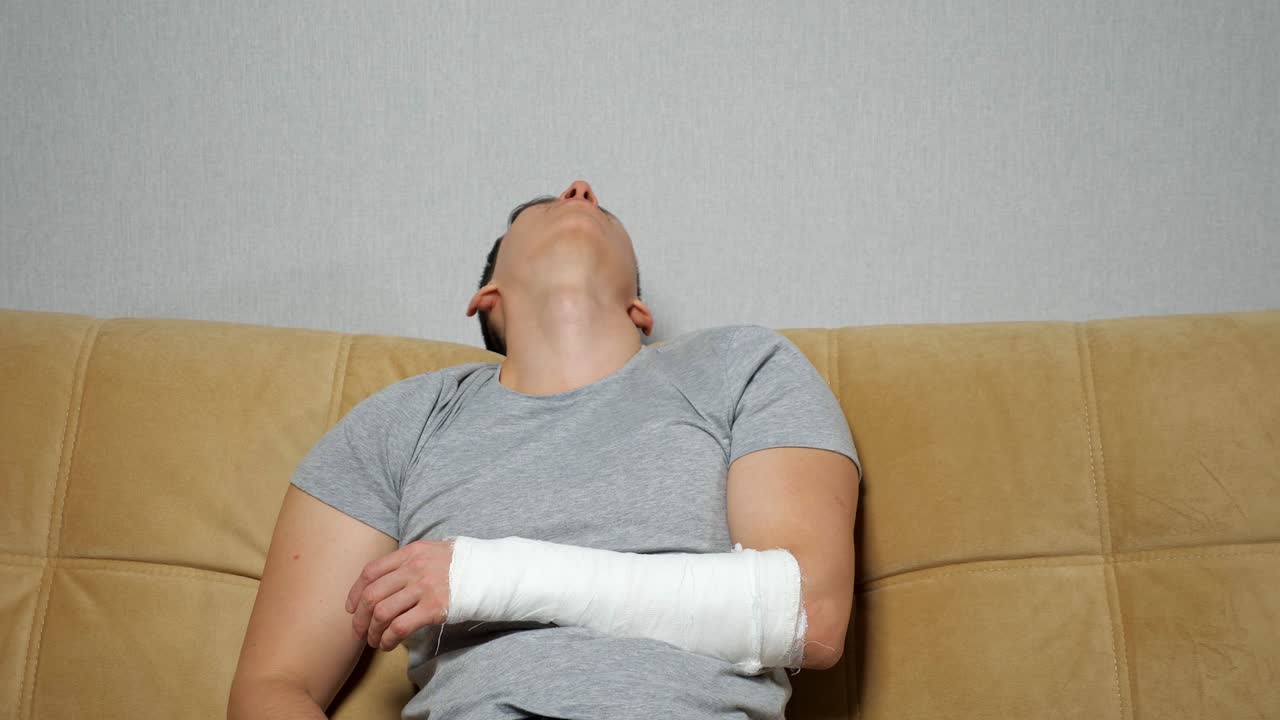 Man touches injured arm in gypsum band and sighs tiredly