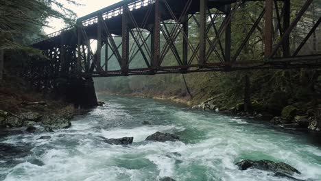 steel railroad bridge spans lewis river, drone flies under just above water