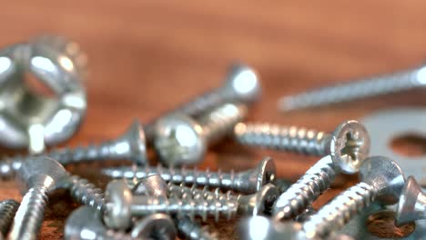 the bunch of steel screws on wooden table. screw production, heap of metal details, close up shot