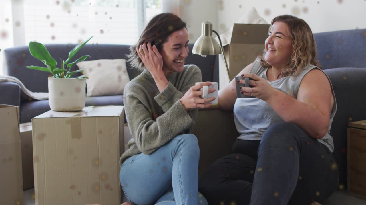 Annuncio pubblicitario lifestyle che mostra due donne che brindano con tazze di caffè dopo essersi trasferite tra scatoloni sul pavimento