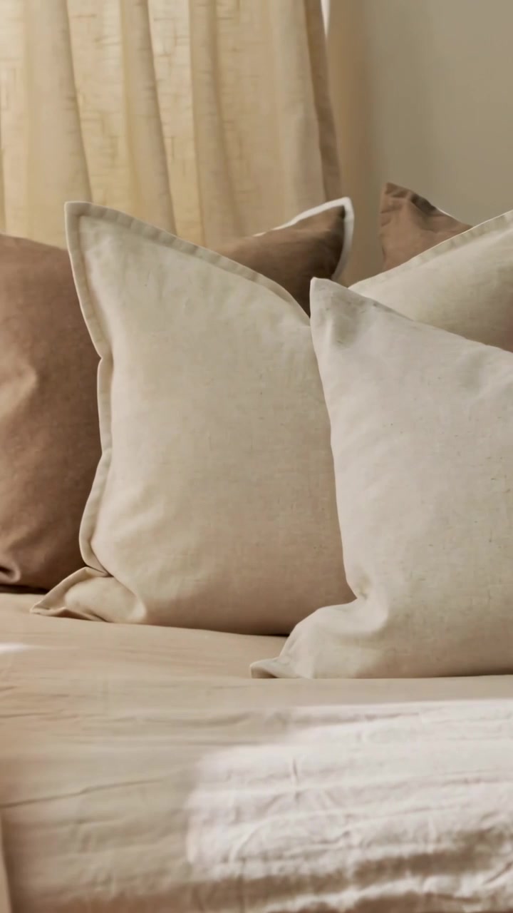 Video verticale: Tenda trasparente che ondeggia, spostata a sinistra dalla brezza, rivelando un cuscino di lino color crema sul letto.