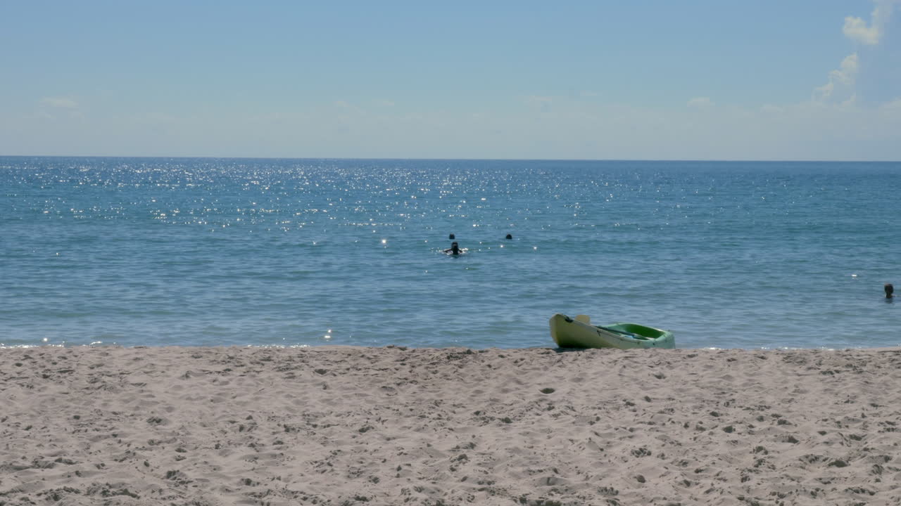 멀리서 사람들이 수영하는 동안 빈 카약이 해변가에 앉아 있다