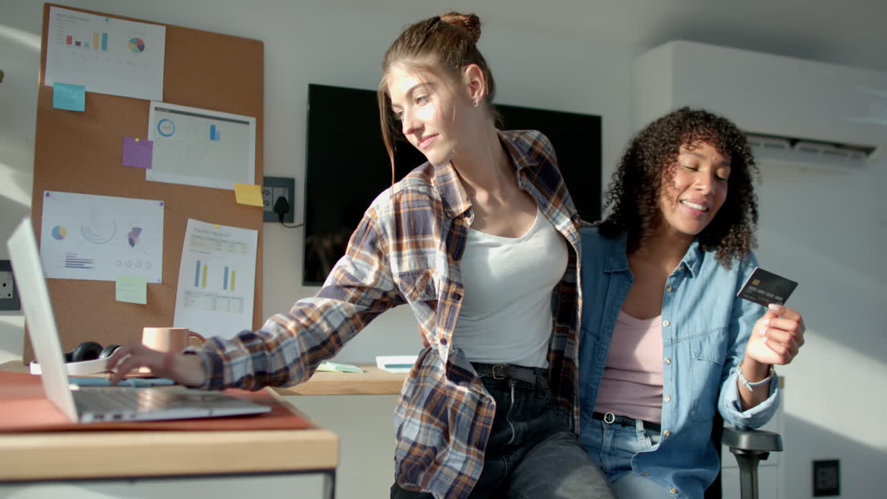Using laptop, lesbian couple shopping online with credit card at home office