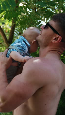 strong caucasian man with naked torso holding a baby on one hand above the head. father is playing with an infant son.. vertical video