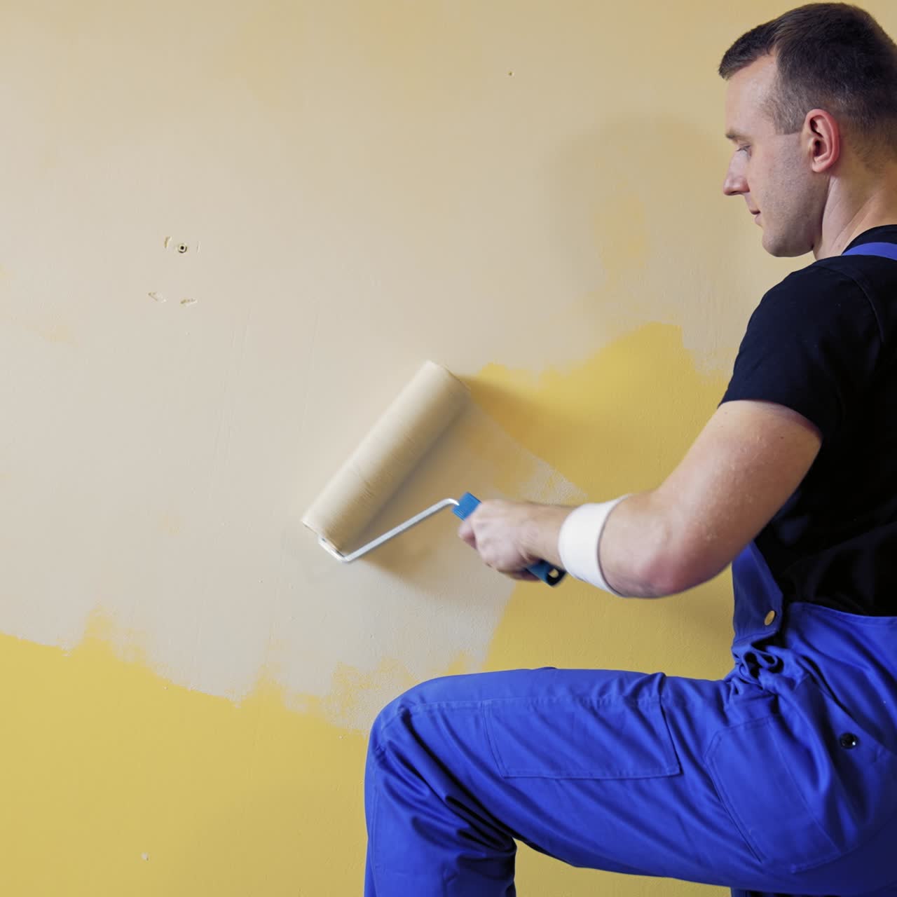 Painter man with a roller brush. Builder at work painting wall. Makeover and renovation indoors. Professional painting services