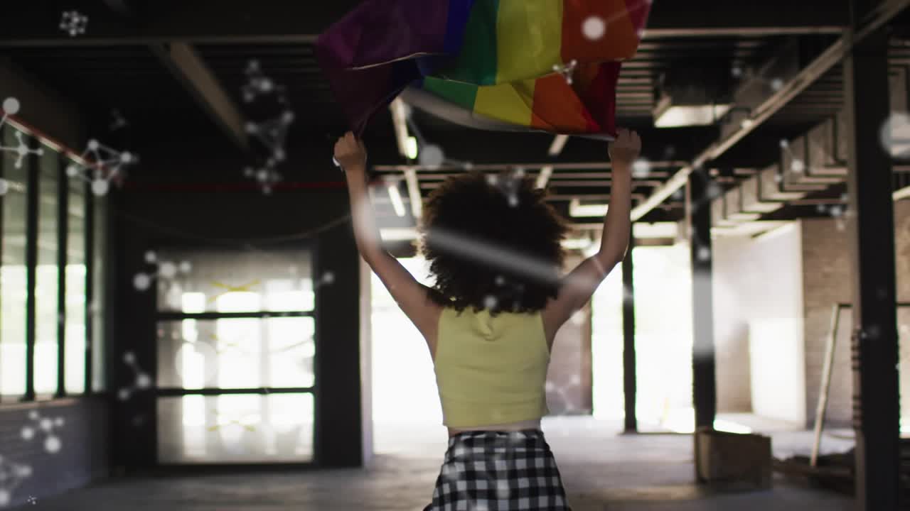 Mujer en un almacén levantando una bandera doblada, agitándola y revelando un arcoíris mientras el resplandor bokeh muestra orgullo