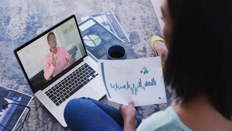 African-american-woman-holding-a-document-having-a-video-call-with-male-colleague-on-laptop