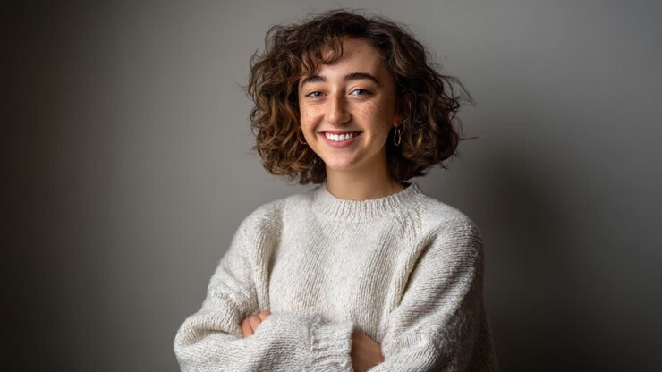 Un sorriso caloroso e accogliente: catturare l'essenza gioiosa di una giovane donna con capelli ricci e un comodo maglione in una morbida luce naturale