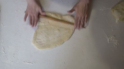 una cocinera enrolla la masa de pizza con un rodillo de madera en la cocina en una mesa de madera. cocinar. la vista desde arriba. primer plano. sin rostro. 4k.