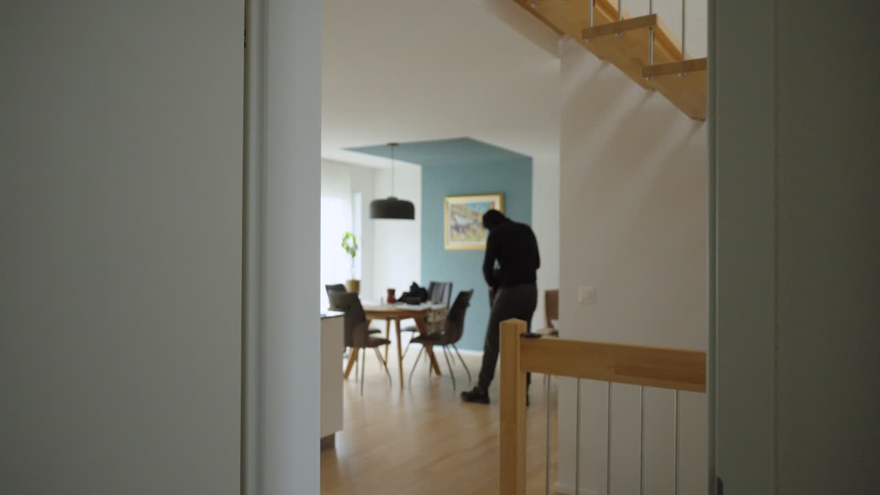 Un ladro si muove in una casa alla luce del giorno e mette oggetti di valore in uno zaino prima di fuggire. Concept per furto, sicurezza domestica, richieste di risarcimento assicurativo e prevenzione della criminalità