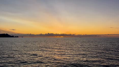 Secluded-island-by-distant-sunset-horizon-at-Vestmannaeyjar,-Iceland,-POV-from-boat-on-open-sea