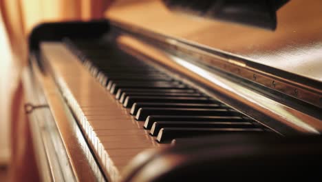 Detail-of-keys-of-an-old-Blüthner-grand-piano-by-large-window-with-curtains,-tripod-rack-focus