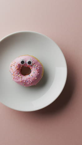 video of donut with icing on white plate over pink background