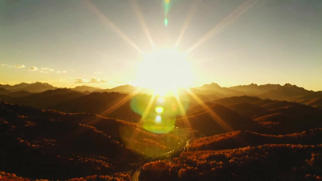 Tilting drone camera moving toward sun over forest valley, capturing golden rays and green flare