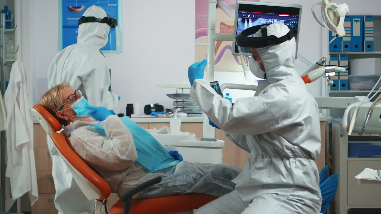 Medico con equipaggiamento protettivo che spiega un problema dentale usando una radiografia