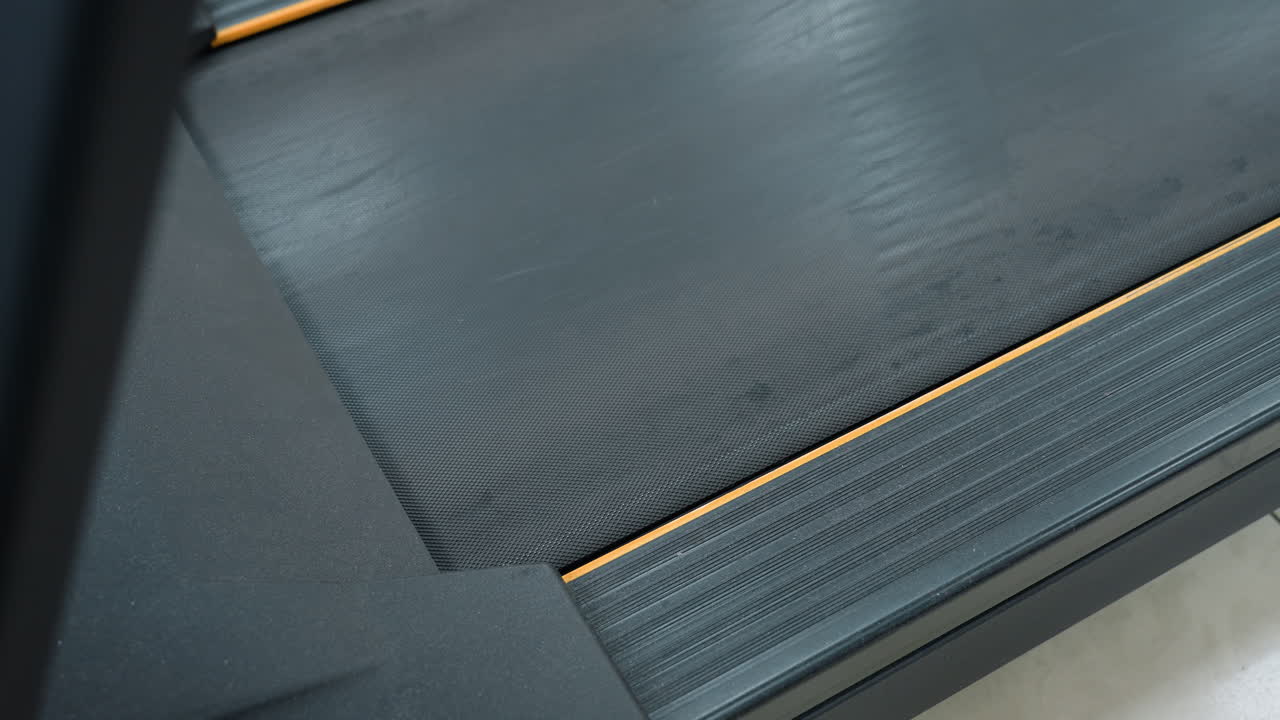 close up treadmill belt slowing to stop after intense workout showing subtle motion fade out and texture details of running surface capturing moment of transition from cardio