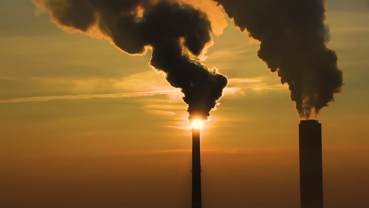 Air pollution. clouds of smoke coming from the chimneys of the plant with beautiful golden yellow lighting of setting sun. Drone flying over smoking smokestacks of a steel factory.