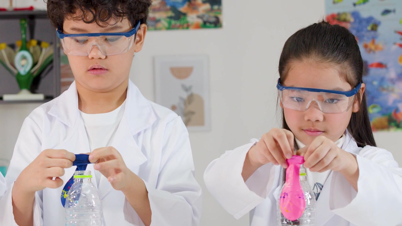 Anak-anak Asia mengenakan jas lab dan kacamata pelindung memasang balon ke botol plastik selama pelajaran sains.