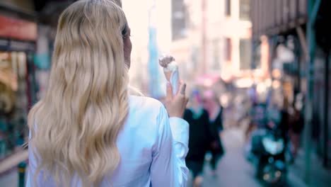 slow motion:young beautiful girl eats ice cream while walking at narrow street in europe