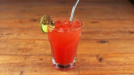 persona colocando un cóctel de maría sangrienta en una mesa de madera, con limón y una paja