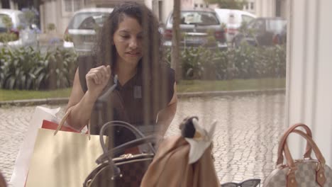 excited latin woman with shopping bags standing at shop window