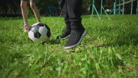 a close-up of people's legs on a grassy field engaged in exercises with a soccer ball in the center, a small child is seen jumping high in the background, with a blurred view of a goal post