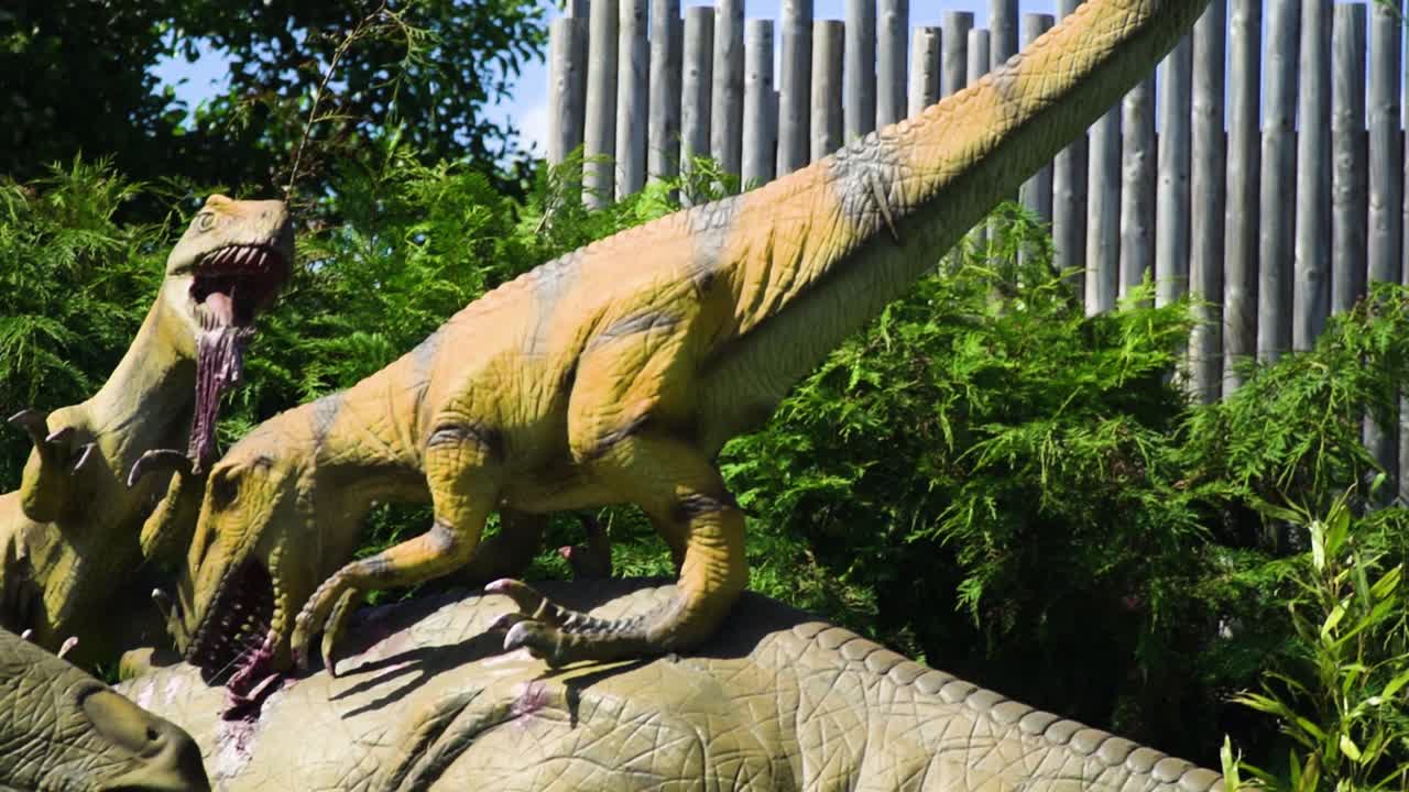 공룡 파충류의 악당 듀오가 동물원 사파리 슬로우 모션에서 더 큰 느린 공룡 모델 가짜 풍경을 공격하고 있습니다.