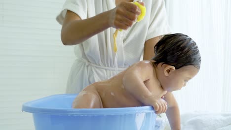 hygienic procedures for newborn, mother bathing her daughter in warm water, bathing the baby in the bathroom. newborn takes a bath in bathtub, baby girl smile happy face while take shower