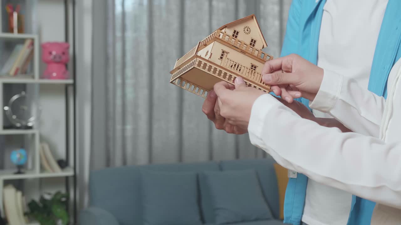 부부의 손으로 집을 판매하는 부동산 중개인으로부터 집 모델을 받습니다.