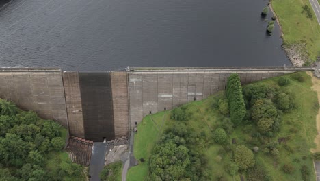 Vista-Aérea-Del-Depósito-De-Madera-De-Stand-Dolly-A-Través-Del-Aliviadero-De-La-Presa-De-Hormigón-Y-El-Lago-De-Agua-Dulce,-West-Yorkshire