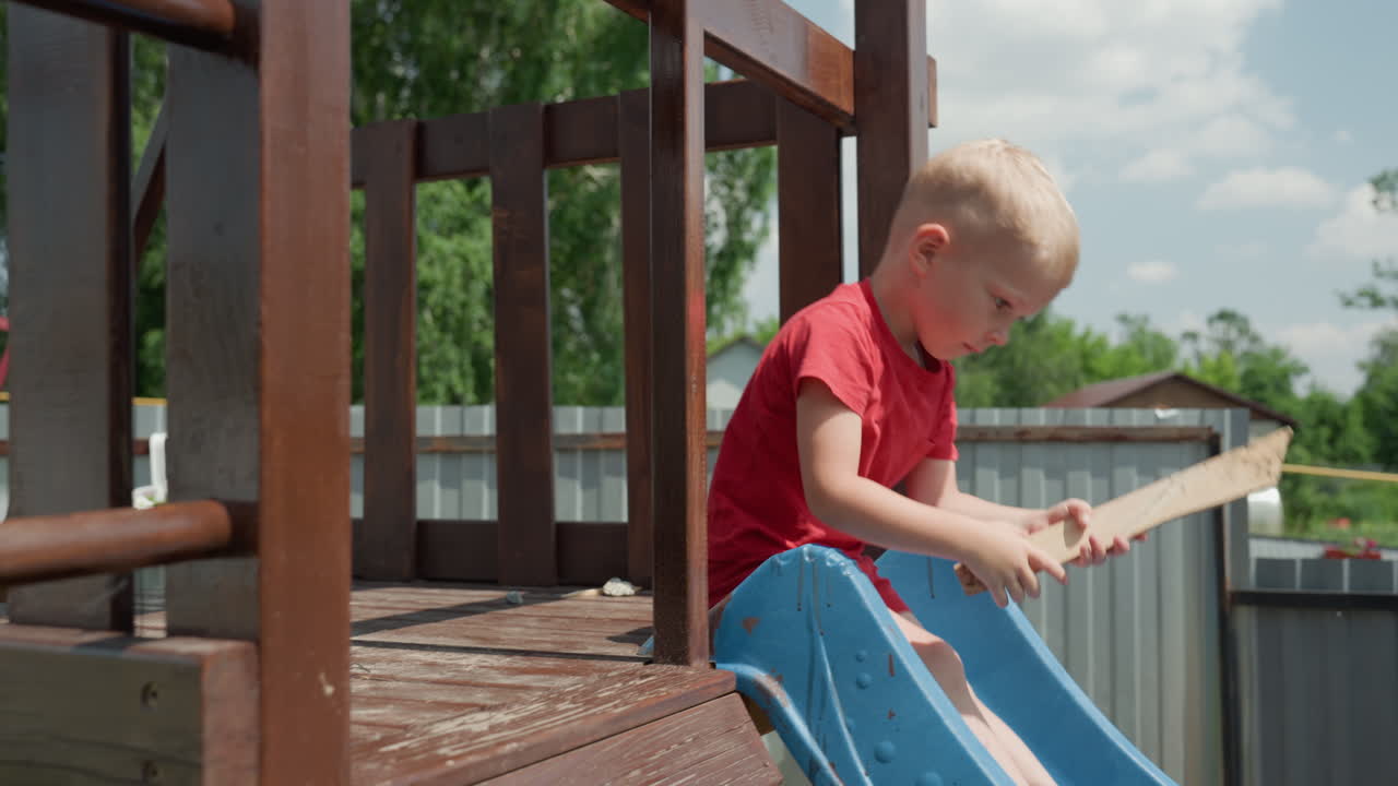 Boy With Blue Slide Enjoys Summer, Young Boy Wearing Red Explores Backyard Surroundings, Boy With Blonde Hair And Focused Expression Explores Small Adventure Near Garden Fence In Backyard