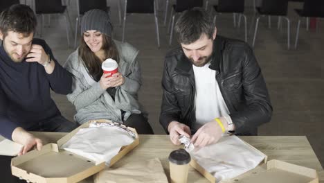 a group of young designers led by the head are working on the project of design office and eating delivered pizza and drinking tea or coffee in paper cups. shot in 4k