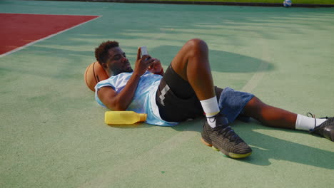 man resting on basketball court, looking at phone