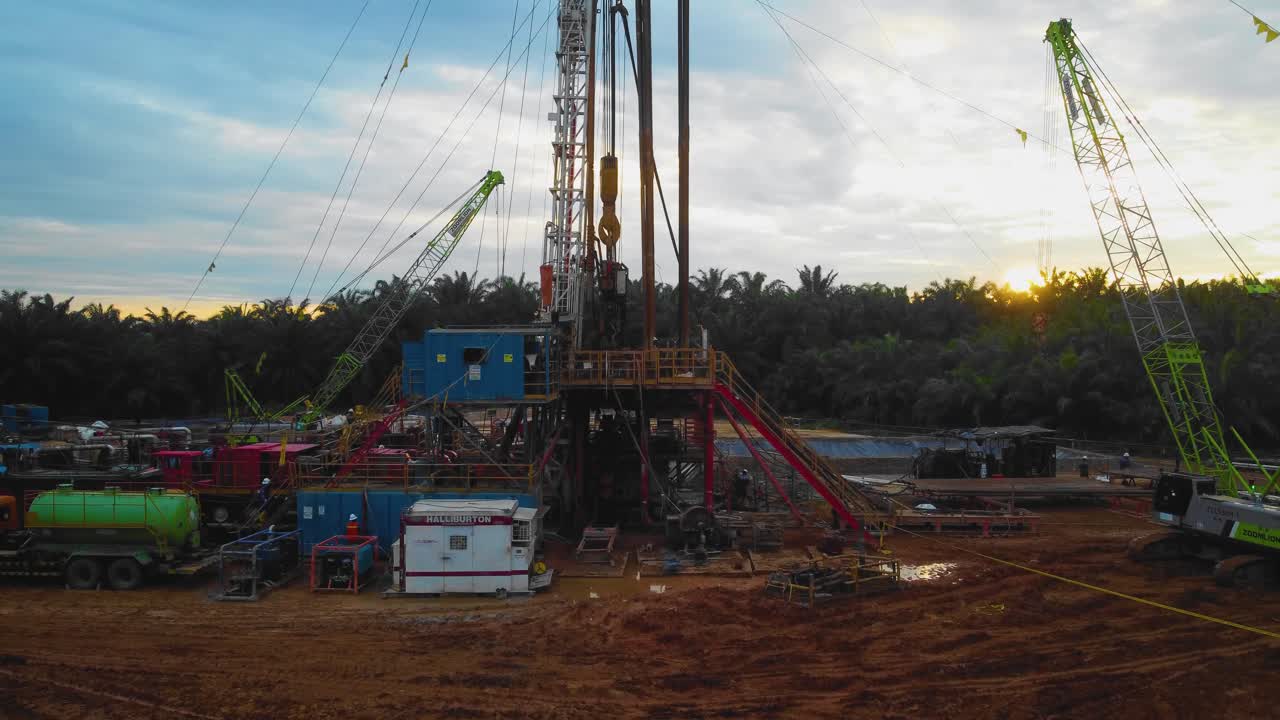 imágenes cinematográficas de drones de la estructura del equipo de la plataforma de perforación en tierra para la exploración y explotación de petróleo en medio de la jungla rodeada de palmeras durante la puesta de sol y el alto precio del petróleo