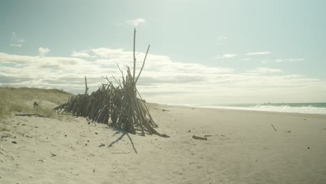 teepee, structure made of wooden sticks, on beach in golden sunshine