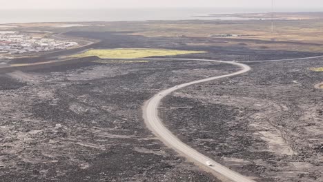 a barren, desolate icelandic landscape featuring a winding road cutting through vast, rugged terrain, dark volcanic ground, sparse vegetation, and distant mountains under an expansive sky.