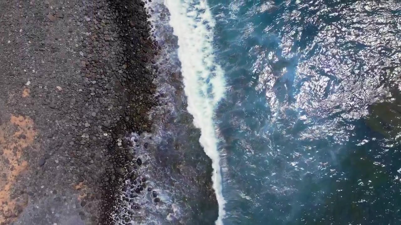Onde si infrangono su una costa rocciosa vulcanica, riprese dall'alto in una giornata di sole.