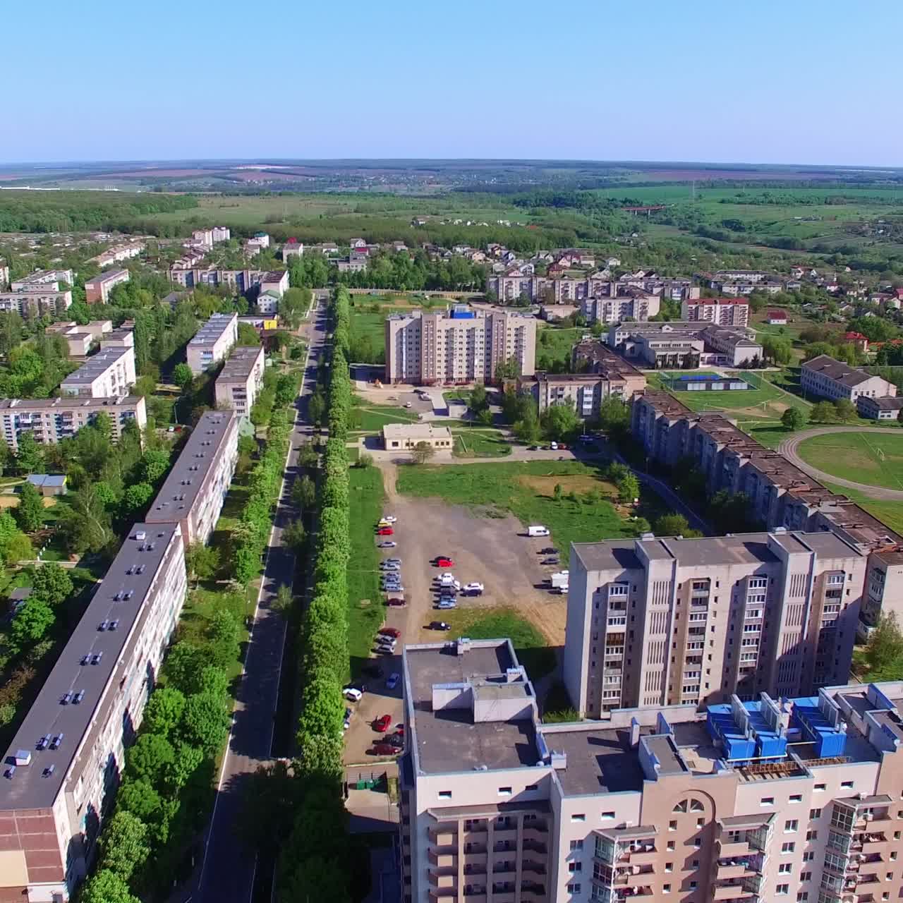 Beautiful architecture of residential area in green city. Drone footage of city at the backdrop of farmlands and blue sky