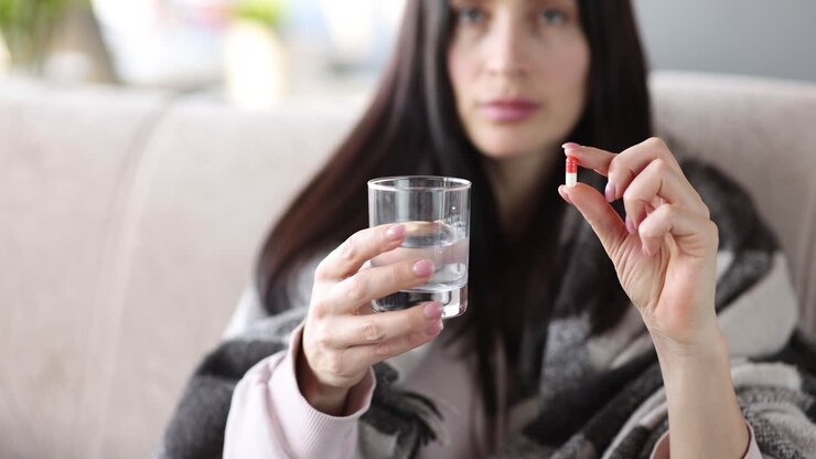 Woman holding a pill and a glass of water, likely for medication