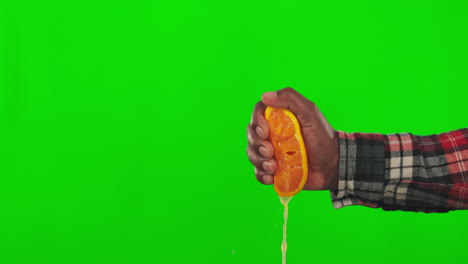 pantalla verde, jugo y una mano apretando una naranja