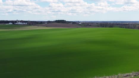 drone shot of green agriculture field crops on picturesque rolling hills and cloudy blue sky