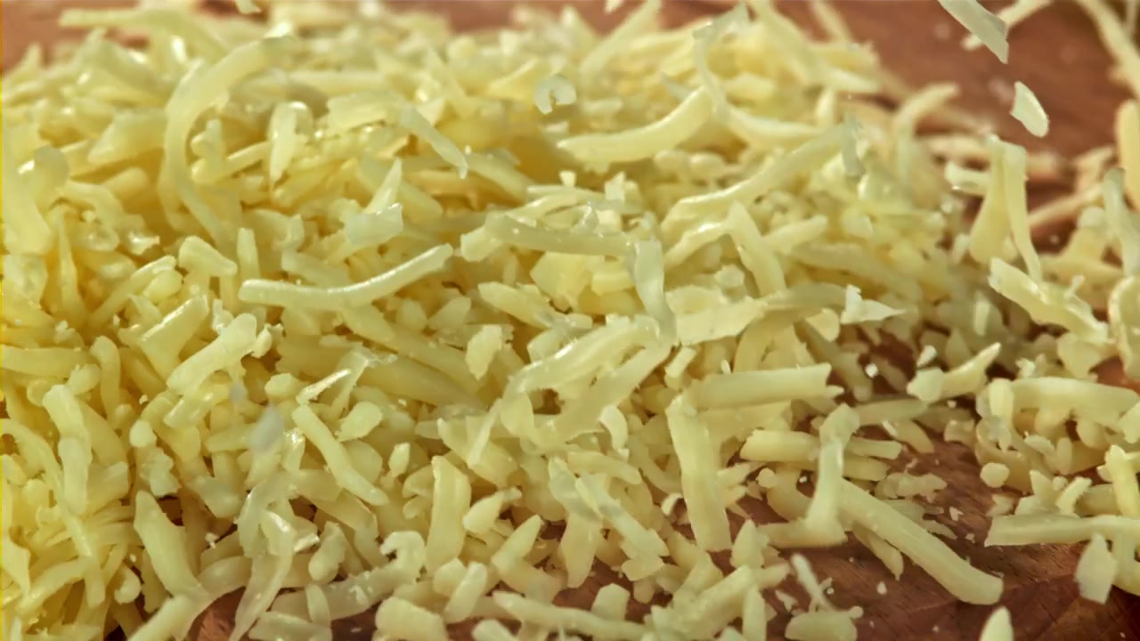 Primo piano di formaggio grattugiato che cade su un tagliere di legno