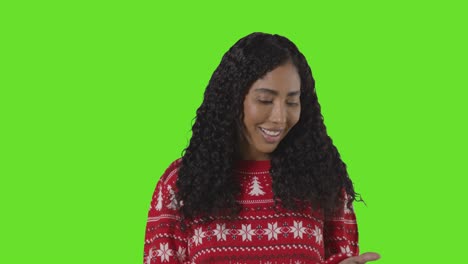 studio portrait of woman wearing christmas jumper against green screen with hands out to catch falling snow 1